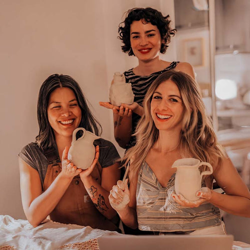 A group of three women holding aloft clay pots made using Sculpd Pottery Kits