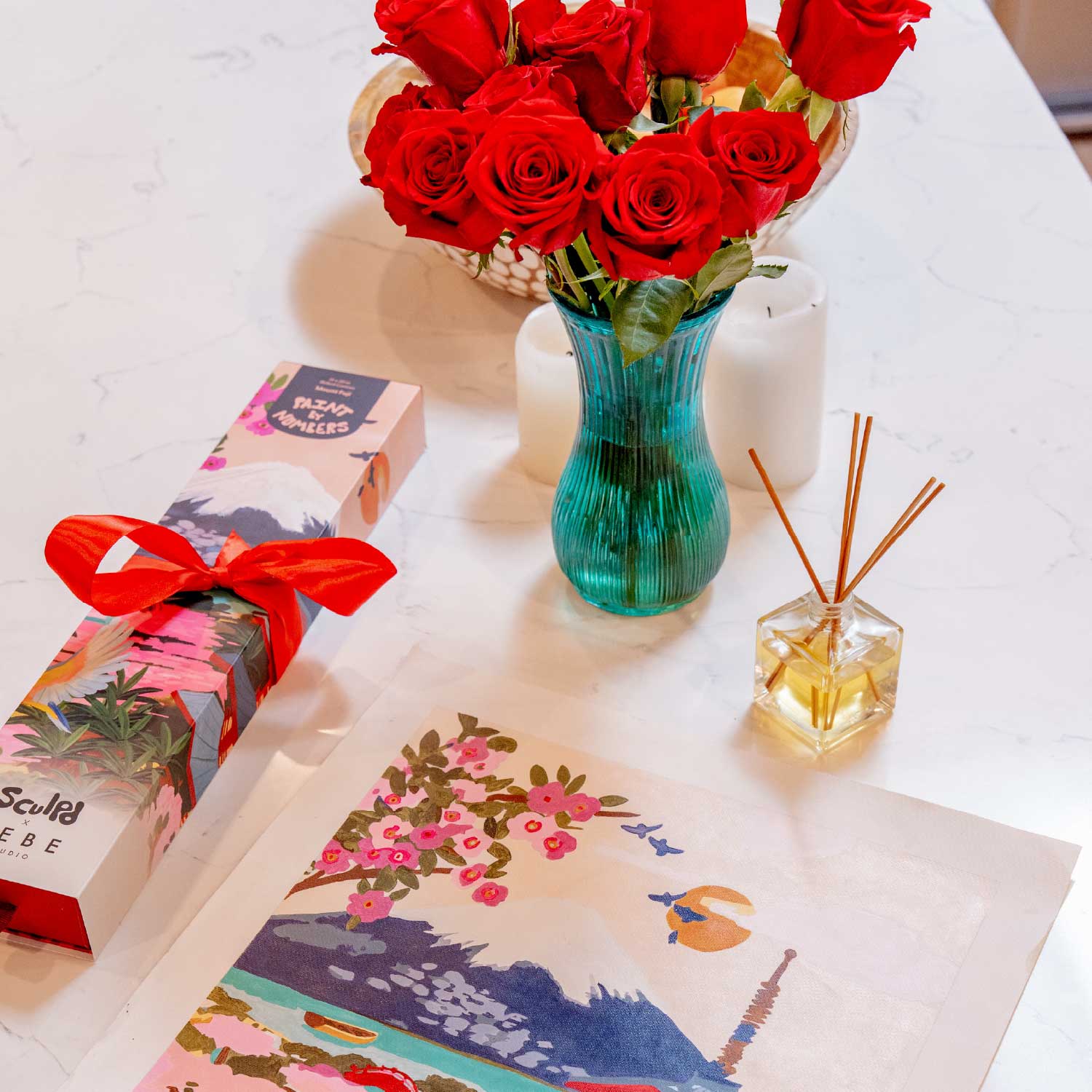 Bouquet of red roses in a blue vase on a table with paint by numbers gift kit