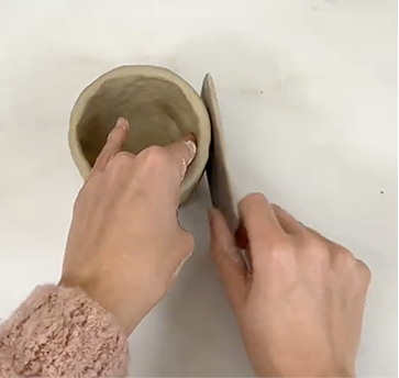 Smoothing the surface of a Sculpd Pinch pot using a wooden tool