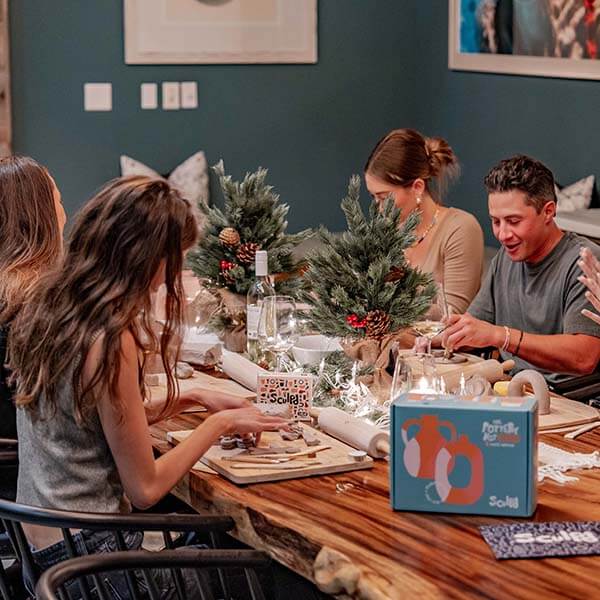 A festive gathering with friends enjoying a Sculpd Pottery Kit night, surrounded by holiday decorations and cozy vibes